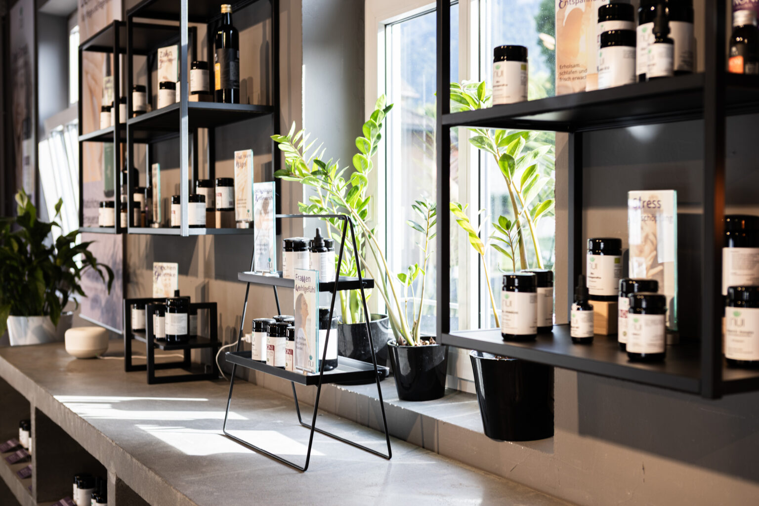 Estanterías junto a la ventana en la tienda NUI de Dornbirn con cápsulas y gotas entre plantas verdes