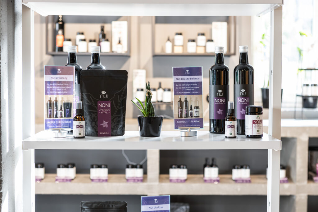 Estantería con botellas NUI NONI Original, bolsa de polvo, espray y cápsulas con las tarjetas de precio
