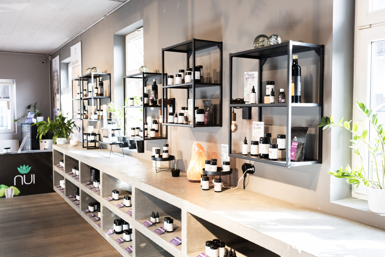 Pared de estanterías en la tienda NUI de Dornbirn con cápsulas, gotas y aceites sobre un largo mostrador de hormigón